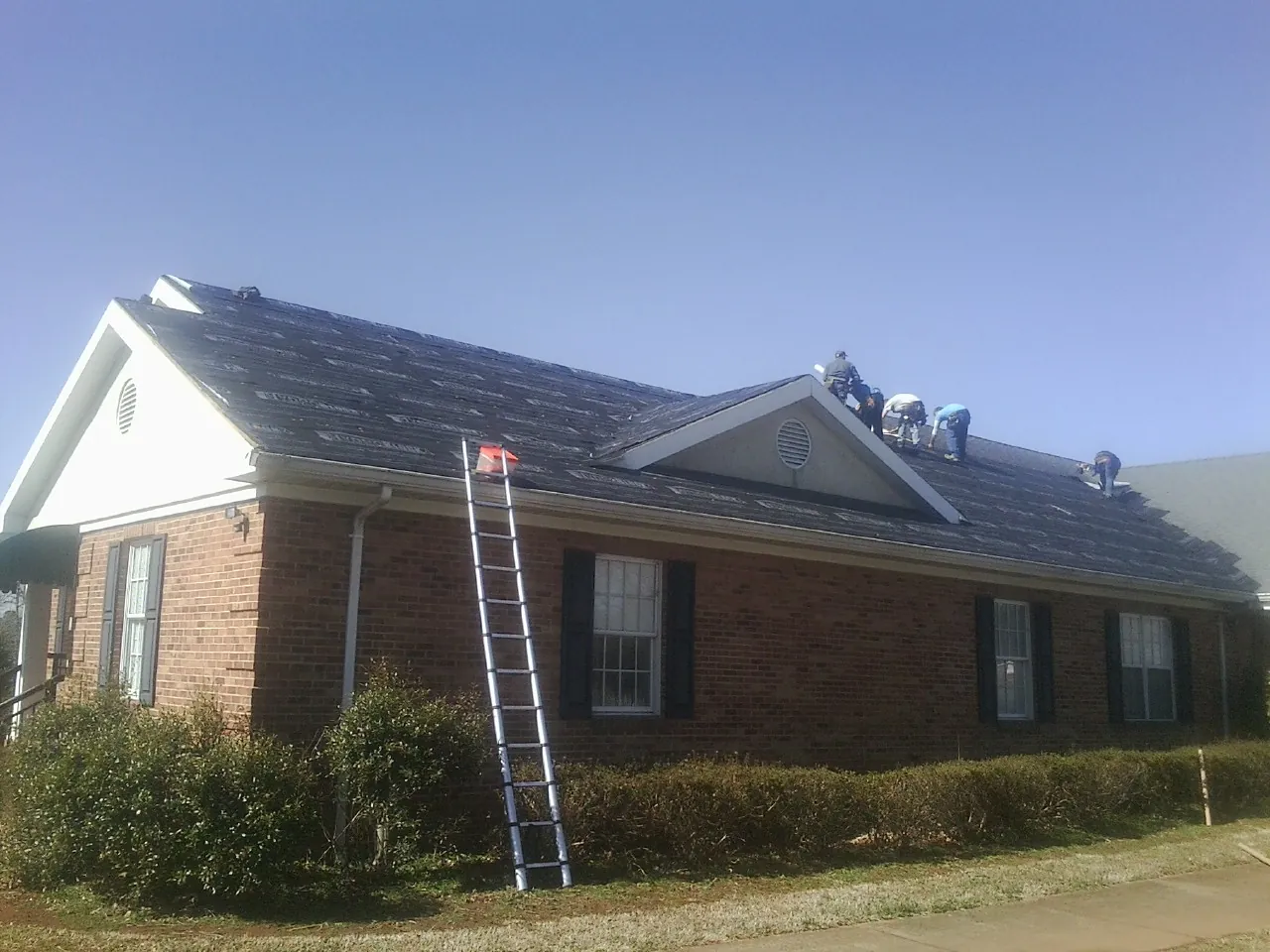 Crew tearing shingles off a brick ranch roof with a ladder set — Emergency Roof Repair work by our crew in Ulster