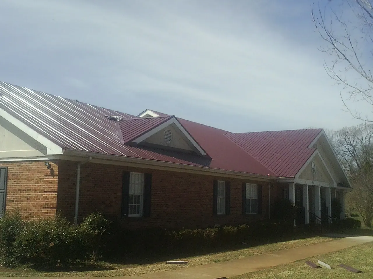 Red metal roof with gabled entries on a long brick building, from a Hail Damage Roof Repair job in Ulster