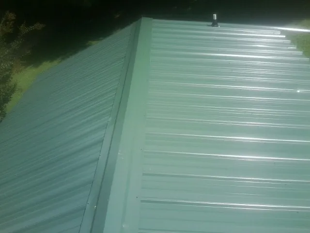 New green metal panels meeting at the ridge of a roof — Flat Roof Repair work by our crew in Ulster