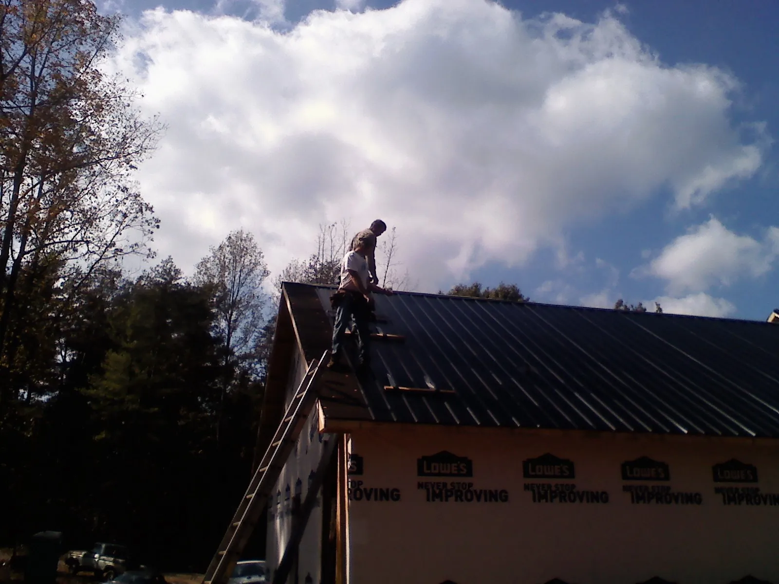 Roofer fastening dark metal panels high against a cloudy sky, from a Roof Inspection job in Ulster