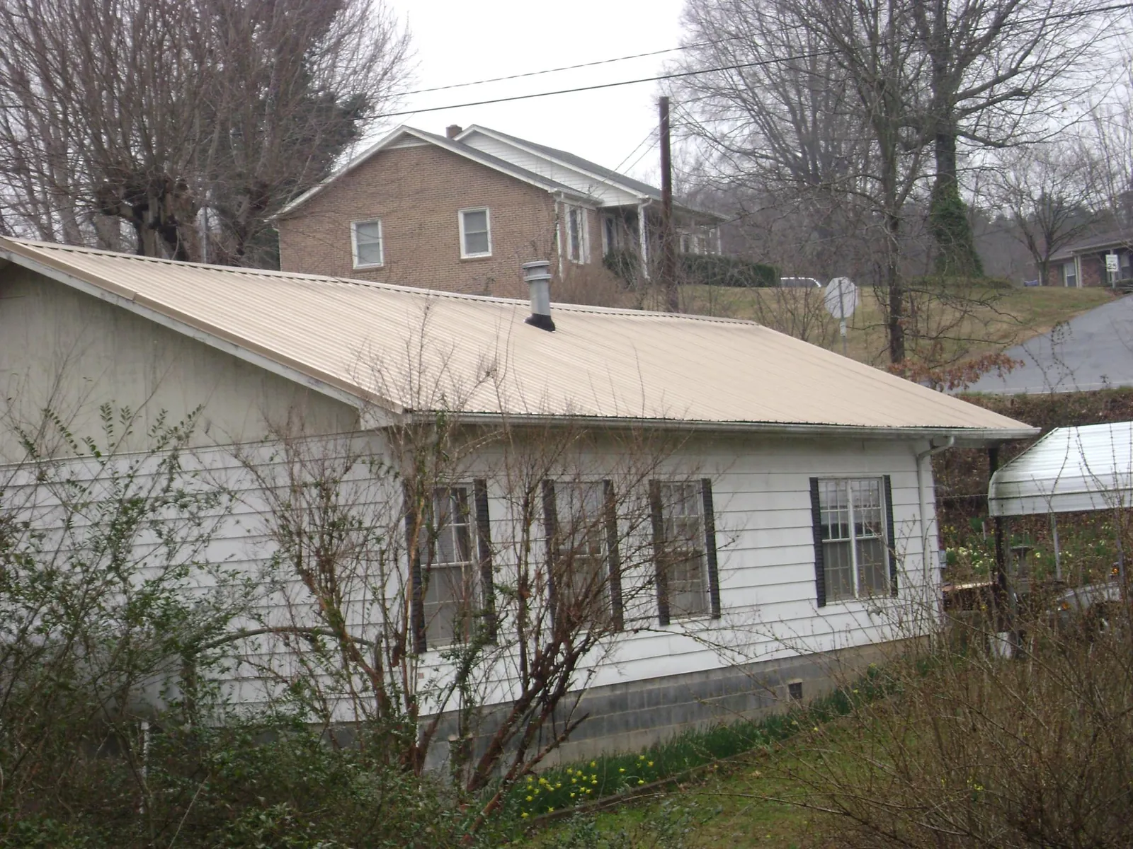 Tan metal roof on a white sided house set into a hillside — Commercial Roofing by Roofing Brothers in Ulster